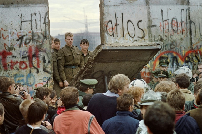 Berlinenses ocidentais se amontoam em frente ao Muro de Berlim enquanto assistem guardas fronteiriços da Alemanha Oriental demolindo uma seção do muro para abrir um novo ponto de passagem entre Berlim Oriental e Ocidental