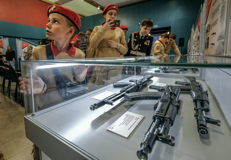 Crianças observam o icônico Kalashnikov em exposição dedicada ao seu inventor.