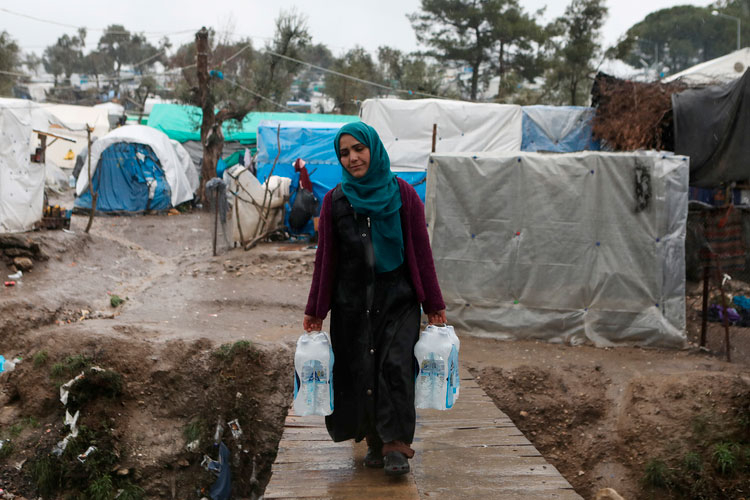 Uma mulher carrega garrafas de água em um campo temporário de refugiados na ilha de Lesbos, Grécia, em 6 de fevereiro de 2020
