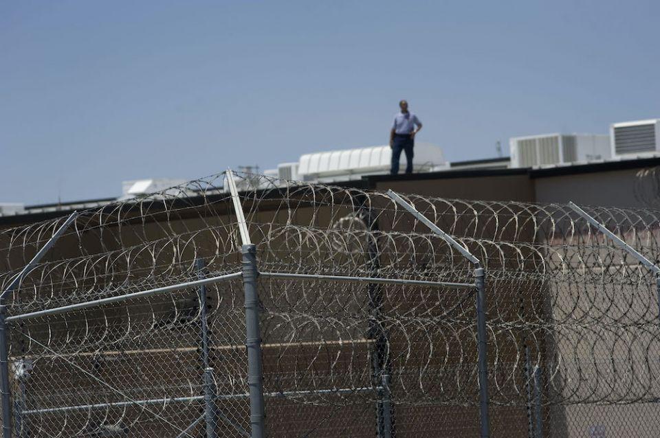 Um homem é retratado sobre um telhado atrás de uma cerca de arame farpado no Centro de Detenção de Otay Mesa para aqueles que entram nos EUA buscando ilegalmente asilo, em San Diego, a 2 de julho de 2019