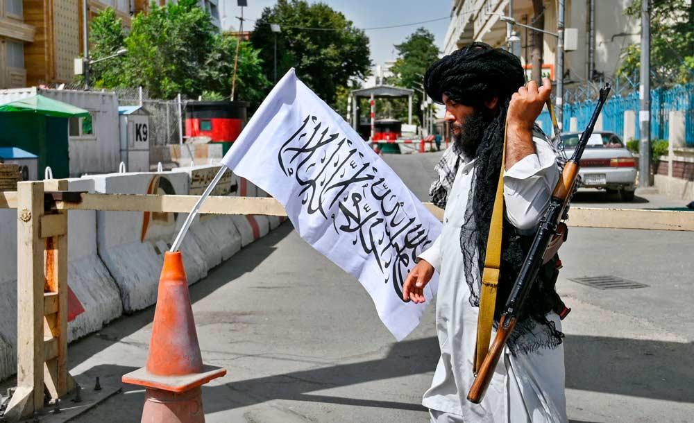 Integrante do Talibã monta guarda em avenida de Cabul ao lado da bandeira do grupo