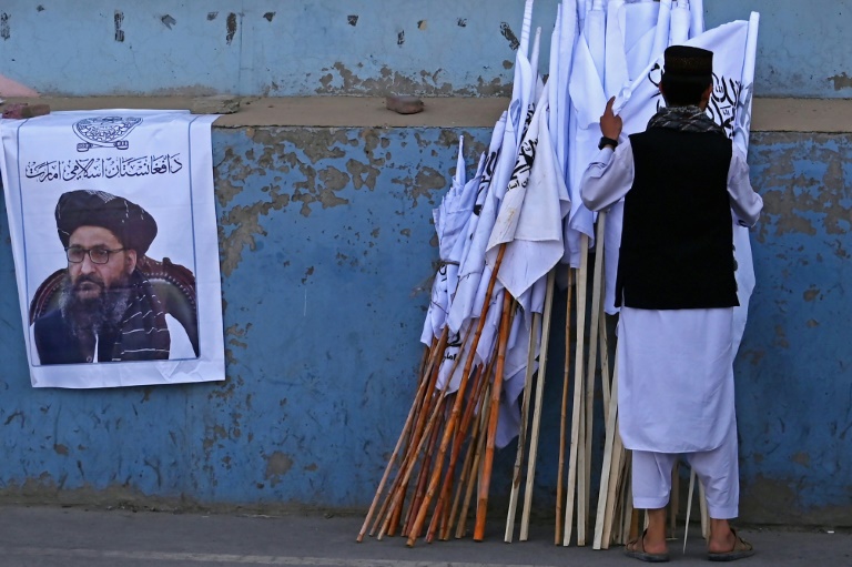 Homem vende bandeiras do Talibã em Cabul, ao lado de cartaz do vice-primeiro-ministro Abdul Ghani Baradar