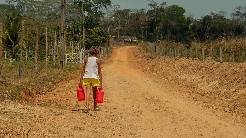 Criança leva recipiente com água coletada da caixa d'água comunitária e leva, andando, até sua casa em Manoel Marques na rodovia Transacreana, imagens da crise hídrica