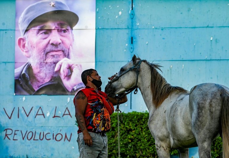 Um homem acaricia seu cavalo ao lado de um pôster do falecido líder cubano Fidel Castro