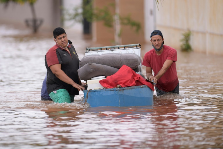 Moradores caminham pela enchente carregando seus pertences em Juatuba, Minas Gerais, em 10 de janeiro de 2022, após chuvas intensas na região