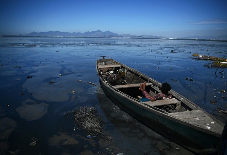 Um homem sentado em um barco cercado por água poluída em um rio que deságua na Baía de Guanabara, no Rio de Janeiro, em março de 2022
