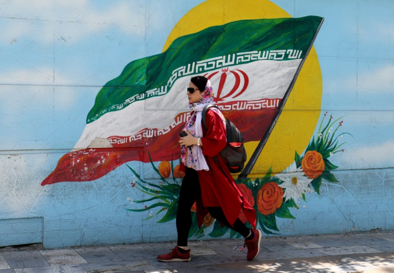 Mulher passa por mural com a bandeira do Irã, em 17 de junho de 2021, em Teerã